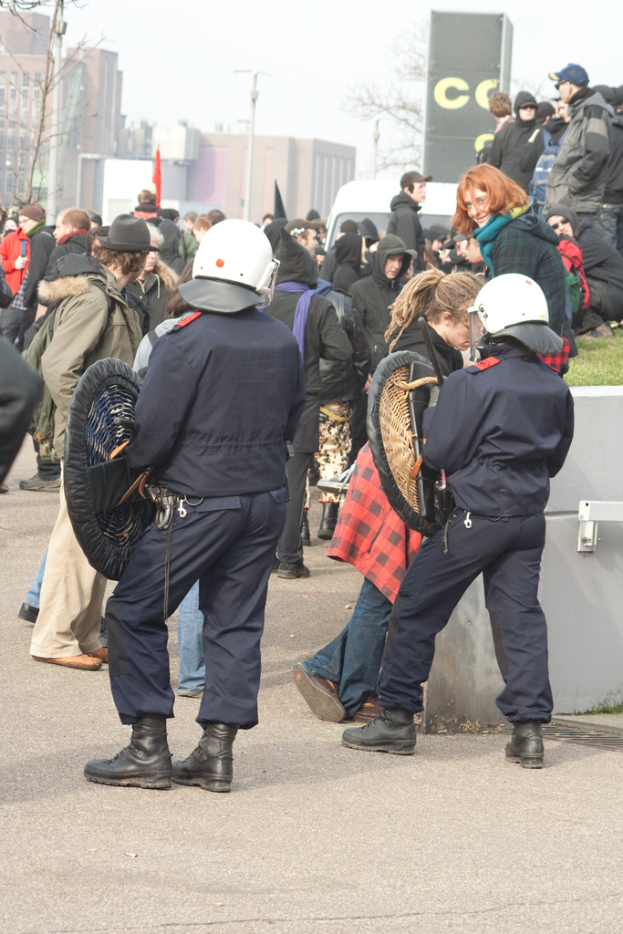 Eine Gruppe von Menschen, die auf einer Straße mit zwei Polizeibeamten vorne, Gebäuden im Hintergrund und Boden unten gehen.
