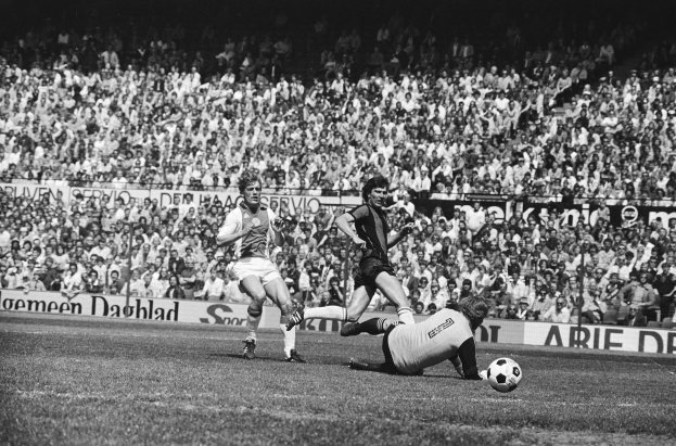 Schwarzes und weißes Foto von Fußballspielern im Einsatz auf einem Feld mit Zuschauern und einem Bundesliga 1978-79 Ajax gegen Hannover 96-Banner im Hintergrund.