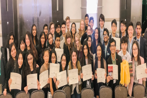 Gruppe von Menschen mit Urkunden in einem Raum mit Stühlen und einer Wand im Hintergrund, wahrscheinlich bei einer Abschlussfeier für das akademische Jahr 2019-2020.