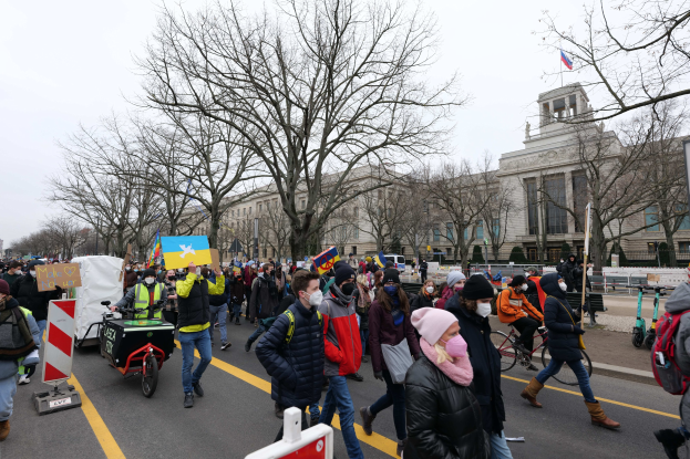 Eine große Gruppe von Menschen nimmt an einer Protestdemo in Washington, D.C. am 21. Januar 2020 teil, geht eine Straße entlang mit Schildern, Bannern und Fahrrädern, vorbei an einem Gebäude mit Schildern, Bäumen und einem klaren blauen Himmel.