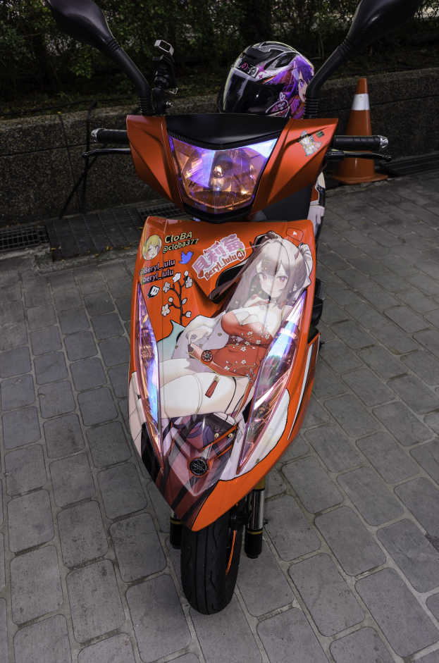 Ein oranges Roller-Fahrzeug, das auf der Seite einer Straße geparkt ist, mit einem Helm darauf, einer Verkehrskegel, einer Wand und Bäumen im Hintergrund.