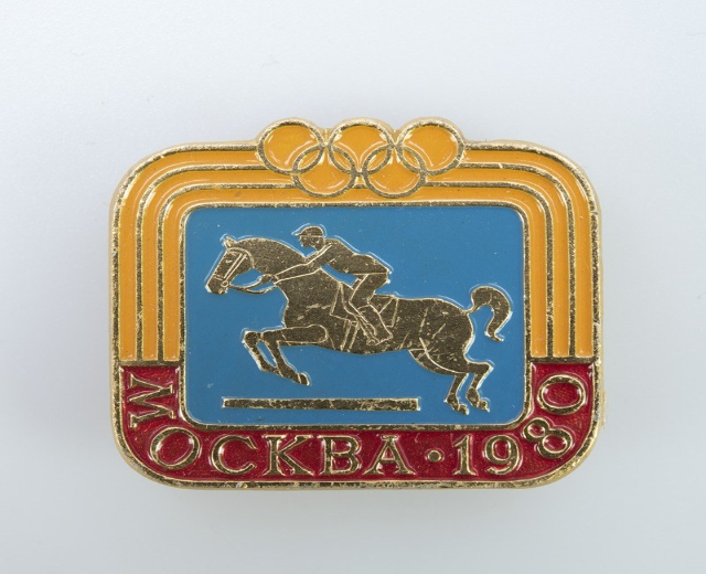 Olympisches Abzeichen von den Olympischen Winterspielen 1988 mit einer Person in weißem Hemd und blauen Shorts auf einem rotbraunen Pferd mit weißer Mähne und Schweif vor einem hellblauen Himmel mit weißen Wolken.