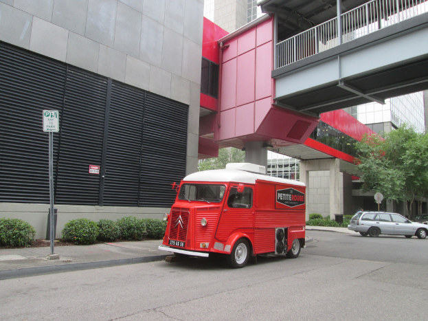 Ein Van steht in der Mitte des Bildes mit einem Auto auf der rechten Seite und Gebäude im Hintergrund.