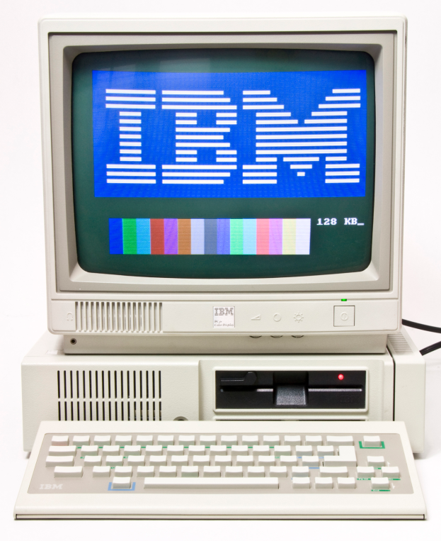 Ein alter IBM-Computer mit einem blauen Bildschirm und einer Tastatur, vor einem weißen Hintergrund.