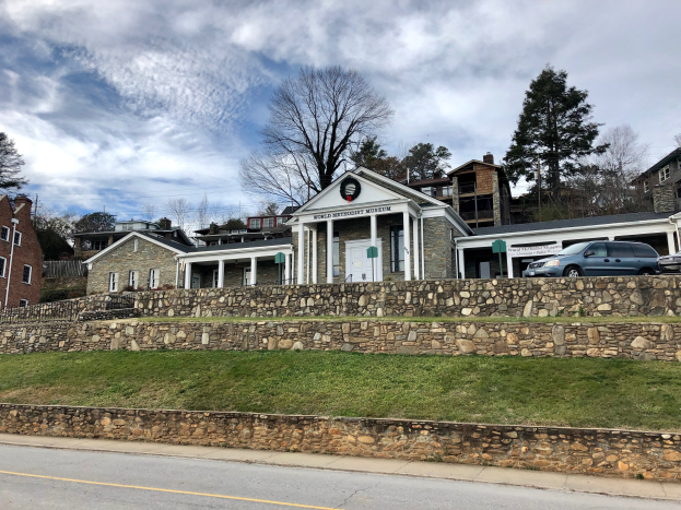 Steinwand mit parkenden Autos, angrenzende Gebäude mit Fenstern und Türen, Bäume und ein bewölkter Himmel im Hintergrund, als das kürzlich wiedereröffnete Weltkulturerbe Museum bezeichnet.
