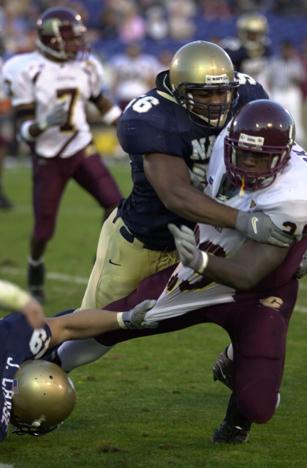 Zwei Fußballspieler in Sportkleidung und Helmen kollidieren auf dem Feld, während andere zuschauen.