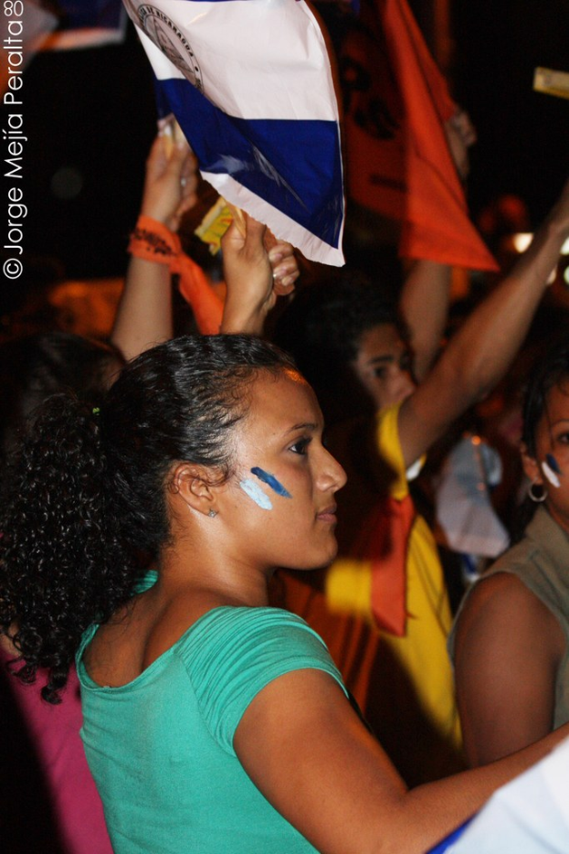 Frauen in grünen T-Shirts bei einer Demonstration, die weiße Schilder in den Händen halten, mit vielen anderen Mädchen im Hintergrund.