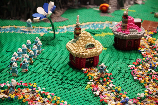 Ein Lego-Modell einer Kleinstadt mit verschiedenen Gebäuden, Pflanzen und Spielzeugen vor einem unscharfen Hintergrund.