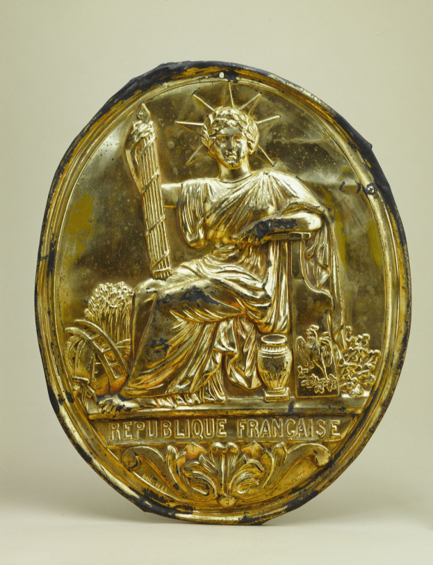 Goldenes rundes Schild mit einer Miniatur-Statue der Freiheitsstatue, darauf eingraviert, auf einem weißen Hintergrund.