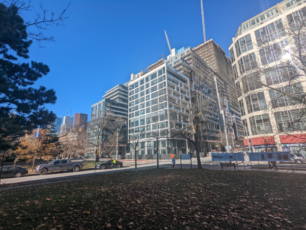 Eine StraÃe in Toronto mit hohen GebÃude, Fahrzeugen, Passanten, BÃumen und trockenen BlÃttern auf dem Boden unter einem sichtbaren Himmel.