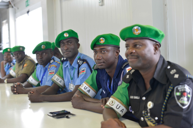 Gruppe von Polizeibeamten sitzt an einem Tisch mit Mobiltelefonen und anderen Gegenständen während einer Schulung in einem Raum mit Fenstern und Deckenbeleuchtung.