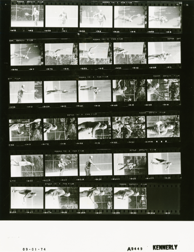 Ein Schwarz-Wei├č-Foto eines Mannes in einem wei├čem Hemd und Shorts, der einen Tennisrahmen in seiner rechten Hand h├Ąlt und einen konzentrierten Ausdruck hat, vor einem Filmstreifen-Hintergrund.