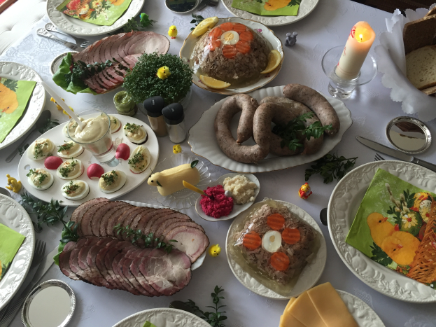 Ein Tisch mit verschiedenen Gerichten, Besteck, Gläsern und Kerzen, umgeben von Stühlen, symbolisiert ein traditionelles deutsches Osteressen.