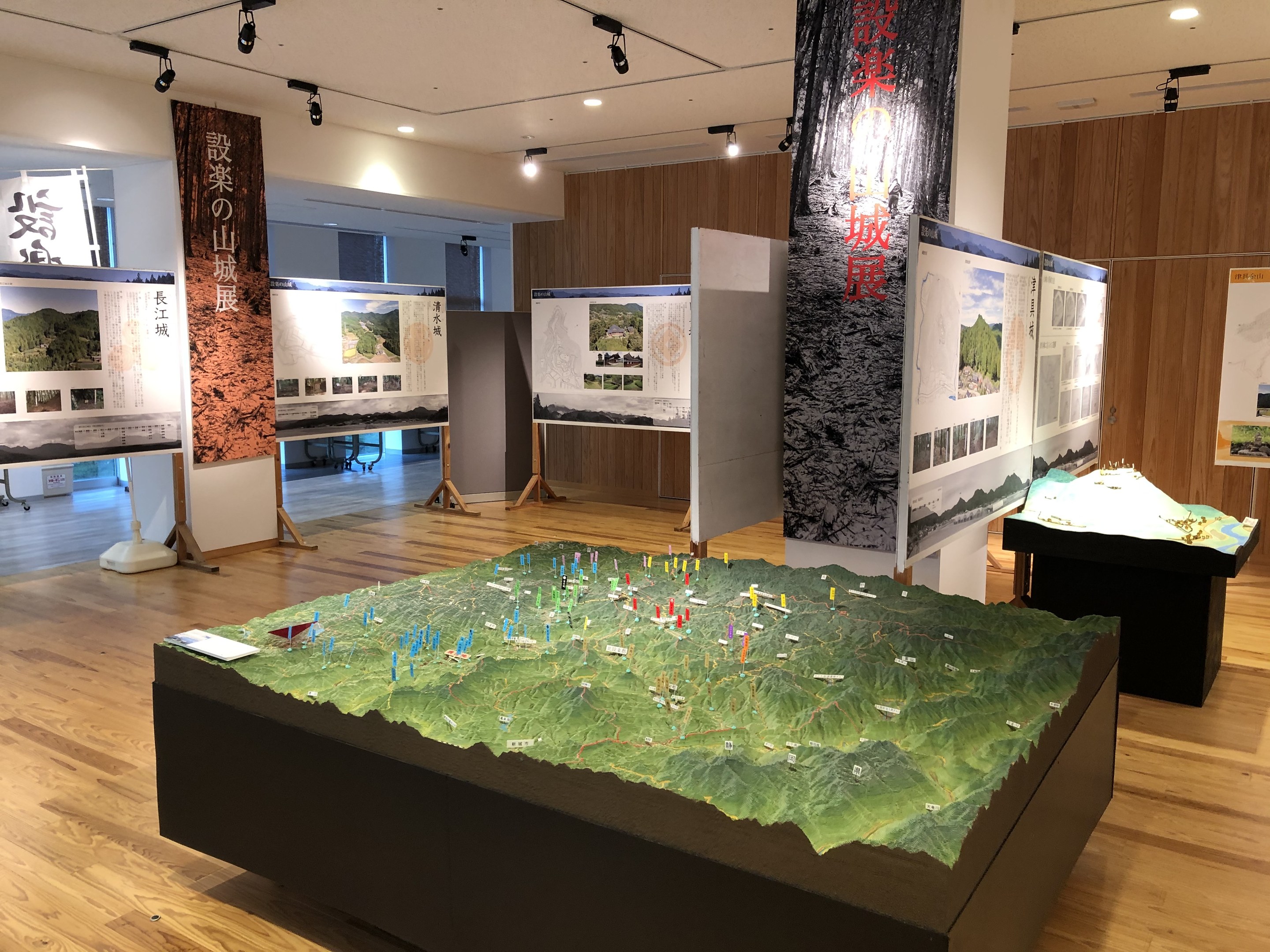 Ausstellungsraum mit verschiedenen historischen Karten Japans, einschließlich Tischkarten, Bannern, Informationsschildern und Deckenbeleuchtung vor einem Holz Hintergrund.