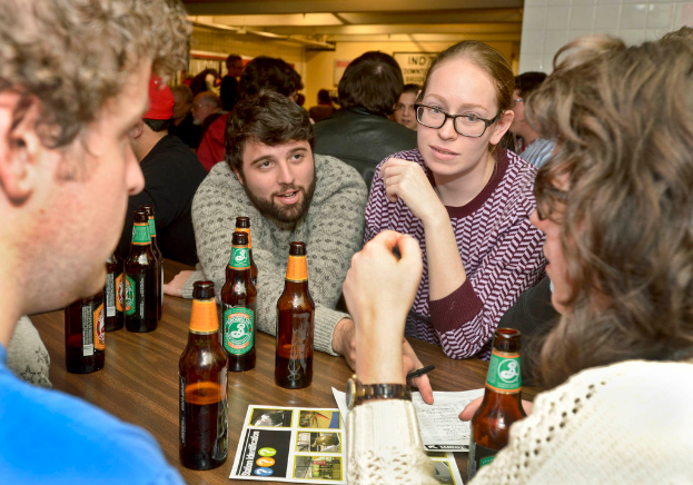 Mehrere Personen auf beiden Seiten eines Tisches mit Bierflaschen in einem scheinbar bar.