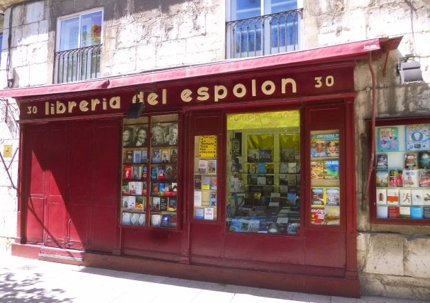 Ein zweistöckiges Gebäude mit einer Schaufensterfront, die ein rotes Vordach mit der Aufschrift "Libreria del Espolon" und ordentlich angeordnete Bücher im Inneren zeigt.