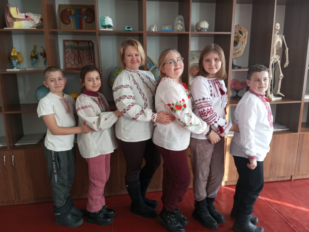 Eine Gruppe von Kindern in traditioneller ukrainischer Kleidung vor einem Bücherregal mit Spielzeug, einem Skelett und anderen Gegenständen