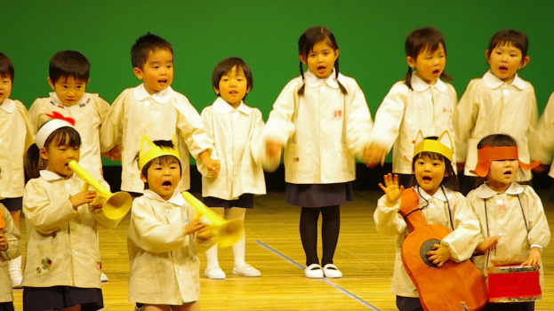 Kinder auf einer B├╝hne singend mit einem gr├╝nen Vorhang im Hintergrund.