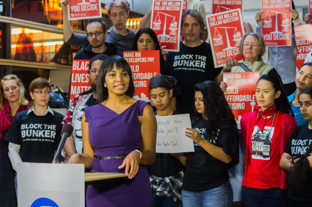 Aktivistin von Black Lives Matter spricht vor einem Publikum mit Schildern, mit Mikrofon und Tafel auf dem Podium.
