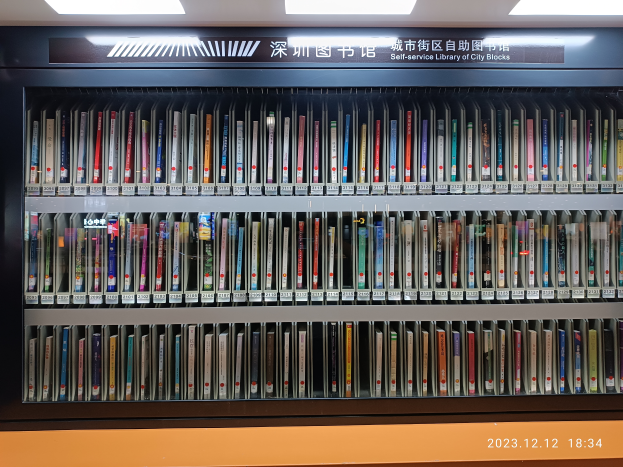 Eine gut beleuchtete Bibliothek mit zahlreichen Büchern auf Regalen, einem Textschild und einem Wasserzeichen unten, die wie eine Selbstbedienungsbibliothek von Stadtvierteln aussieht.