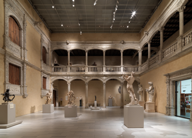 Große Museumsgalerie mit zahlreichen Statuen und Skulpturen auf Sockeln, architektonischen Elementen wie Wänden, Säulen und Geländern, Deckenleuchten und einigen Besuchern.