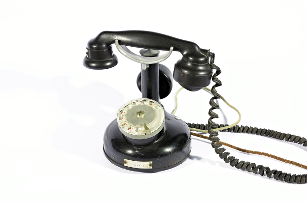 Ein schwarzes Telefon mit Zahlen und Text, der durch die Scheibe sichtbar ist, verbunden durch Kabel, vor einem weißen Hintergrund.