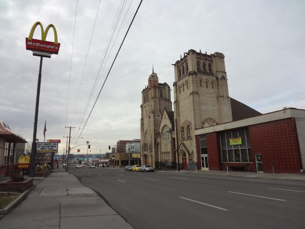 Eine Straßenansicht mit Gebäuden auf der rechten Seite, Masten und Autos in der Mitte und einem McDonald's-Mast auf der linken Seite.