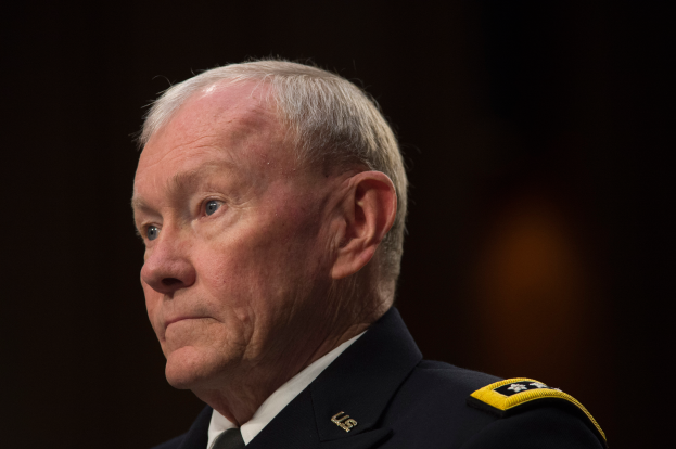 Ein Mann in militärischer Uniform sitzt an einem Tisch mit dunklem Hintergrund, als Verteidigungsminister identifiziert durch den Text am unteren Bildrand.