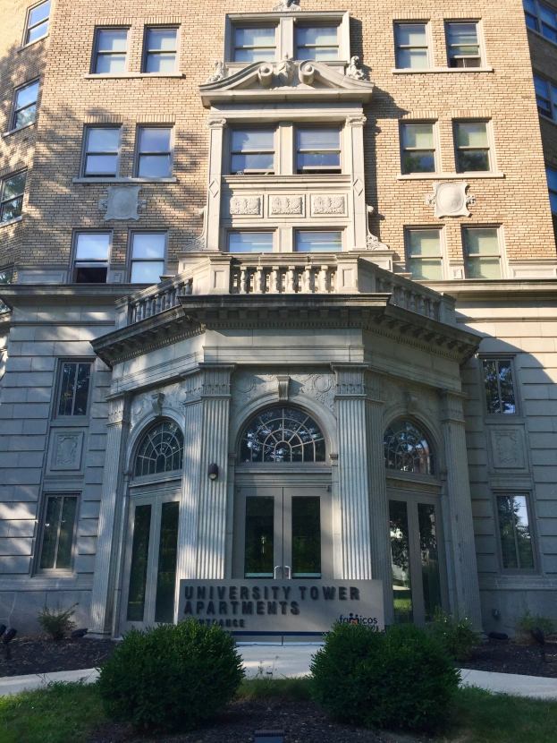 Gro├čes Glasgeb├Ąude mit der Aufschrift "University Tower Apartments" in Chicago, mit grüner Landschaft und einem Schild davor.