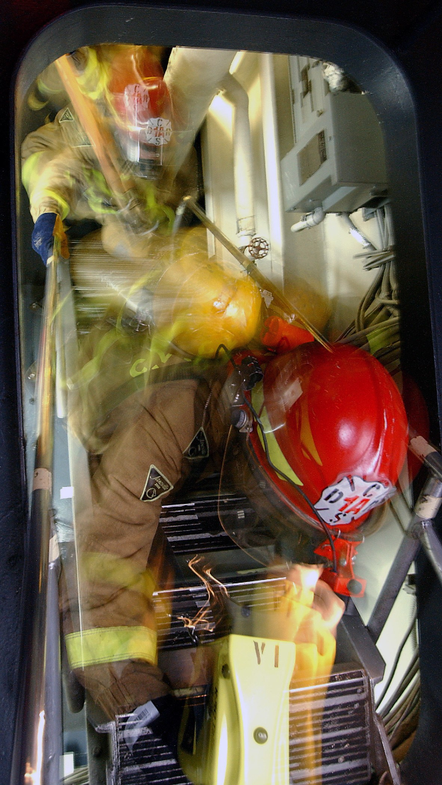 Feuerwehrmann in Schutzausrüstung mit Feuerlöscher und einem anderen Objekt, mit Kabeln und Hintergrunddetails.