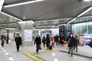Menschen mit Gepäck durch einen Bahnhof gehen, überirdische Schilder und Deckenbeleuchtung.
