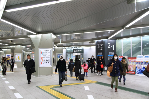 Menschen mit Gepäck durch einen Bahnhof gehen, überirdische Schilder und Deckenbeleuchtung.