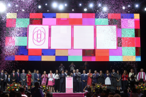Gruppe von Menschen auf einer Bühne mit einem Podium, Blumengestecken, Kameras und einem großen Bildschirm mit Lichtern für die Eröffnungszeremonie des 2018 China International Film Festivals.