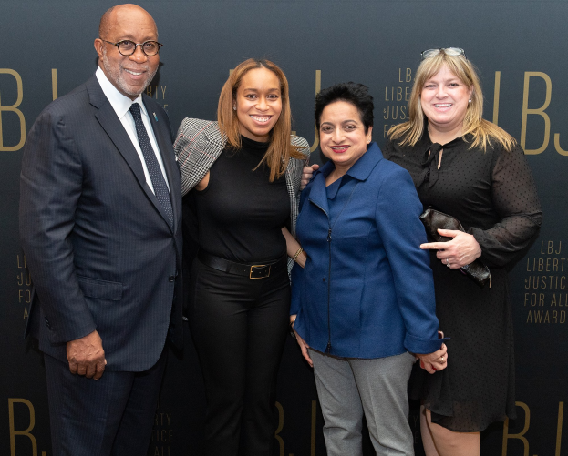 Eine Gruppe von vier Menschen auf einem roten Teppich, die lächeln und für ein Foto posieren, mit einem "Liberty Justice for All Awards"-Schild im Hintergrund.