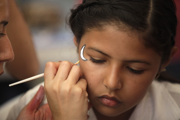 Ein Make-up-Künstler trägt Make-up mit einem Pinsel auf das Gesicht eines jungen Mädchens auf, während der Hintergrund unscharf ist.