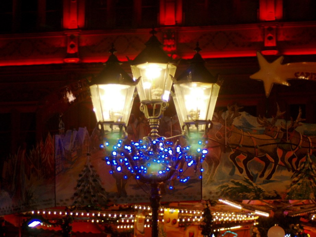Eine mit Lichtern und Dekoration geschmückte Straßenlaterne in einer Stadt bei Nacht, mit einem Gebäude im Hintergrund.