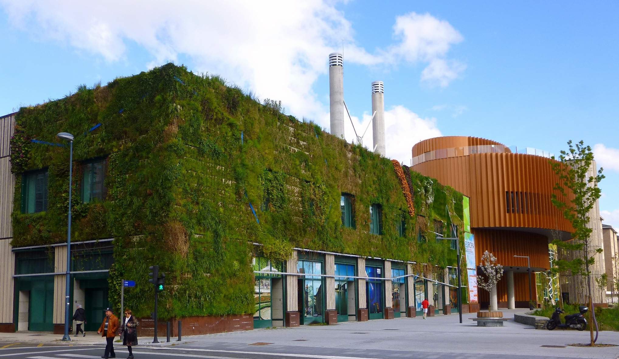 Große nachhaltige Gebäude mit einer Green Wall, umgeben von Straßeninfrastruktur, Fahrzeugen, Füpfchen, Bäumen und einem bewölktem Himmel.