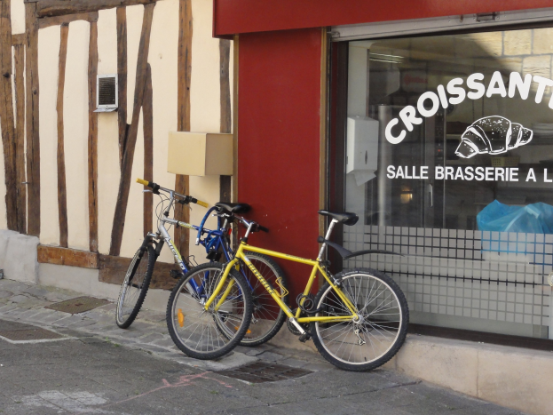 Zwei Fahrr√°der nebeneinander auf einem Gehweg vor einem Laden mit einer Glaswand mit Text und einem Objekt links von den Fahrr√°dern.