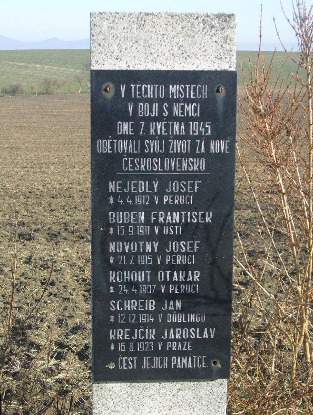 Ein Denkmal mit einer Plakette, auf der "V Techno Mistech" steht, befindet sich in einem Feld und ist von Pflanzen und Hügeln umgeben, während der Himmel klar und blau ist.