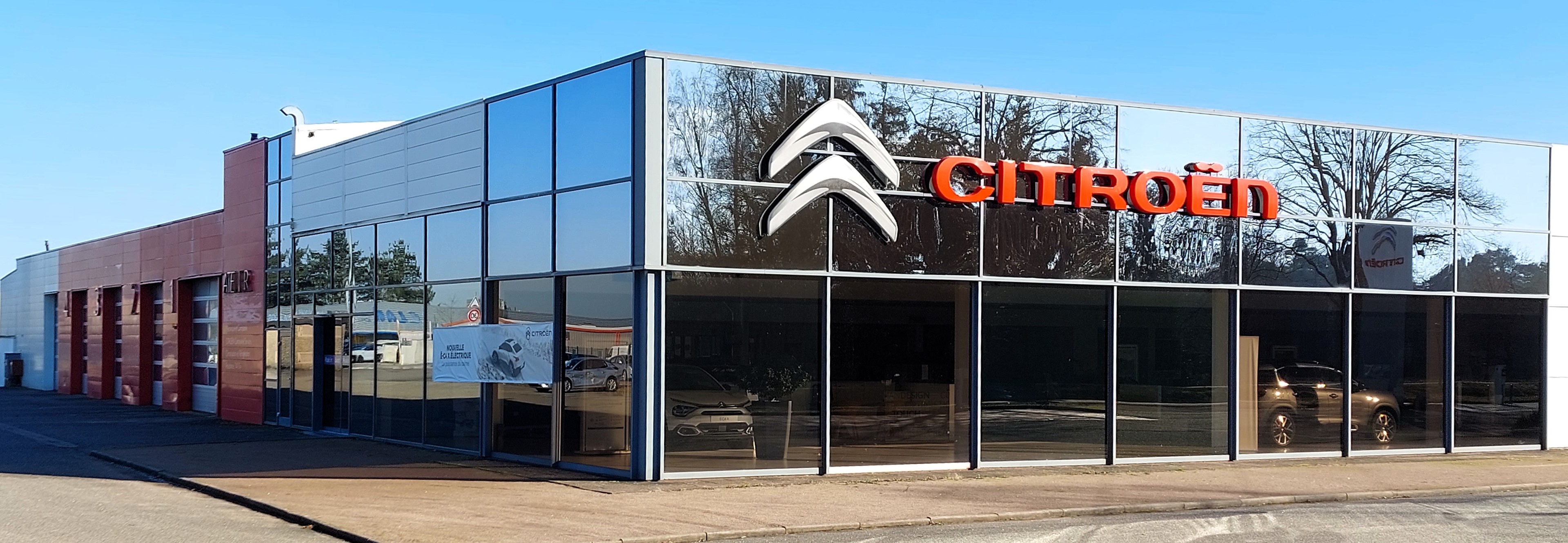 Außenansicht eines Citroën-Autohauses mit Glaswänden und -türen, einer Straße davor und einem klaren blauen Himmel.