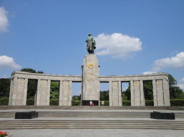 Ein Denkmal mit S├Ąulen und einer Statue ├Âber ihnen, umgeben von B├Ąumen und einem bew├Âlktem Himmel, mit Stufen, die hinauff├╝hren.