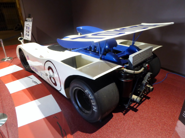 Ein wei├č-blaues Rennauto in einem Museums Setting auf der Goodwood Festival of Speed, umgeben von Barrieren und Informationsschildern.