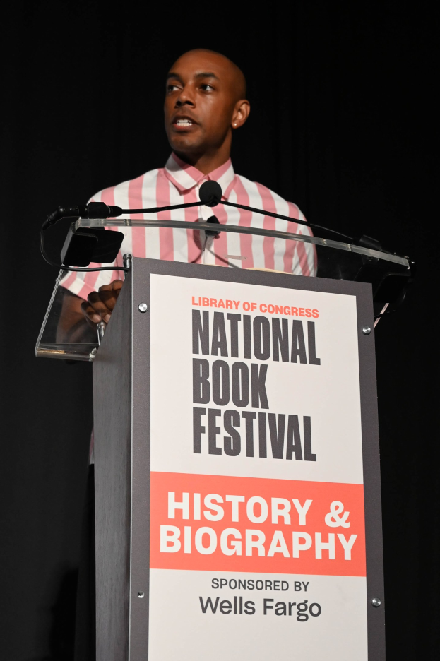 Ein Mann spricht an einem Podium mit einem Mikrofon, während er vor einem Schild mit der Aufschrift "National Book Festival Geschichte & Biografie" steht.