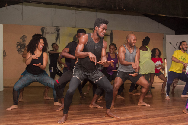 Eine Gruppe von Menschen tanzt in einem Choreografie-Kurs an der Universität Chicago, mit einer Wand voller Gemälde im Hintergrund und einer Decke darüber.