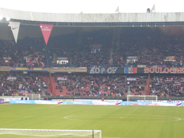 Ein grünes Stadion mit Torstützen auf beiden Seiten, Zuschauern im Hintergrund und zahlreichen Werbetafeln in der Mitte und oben.