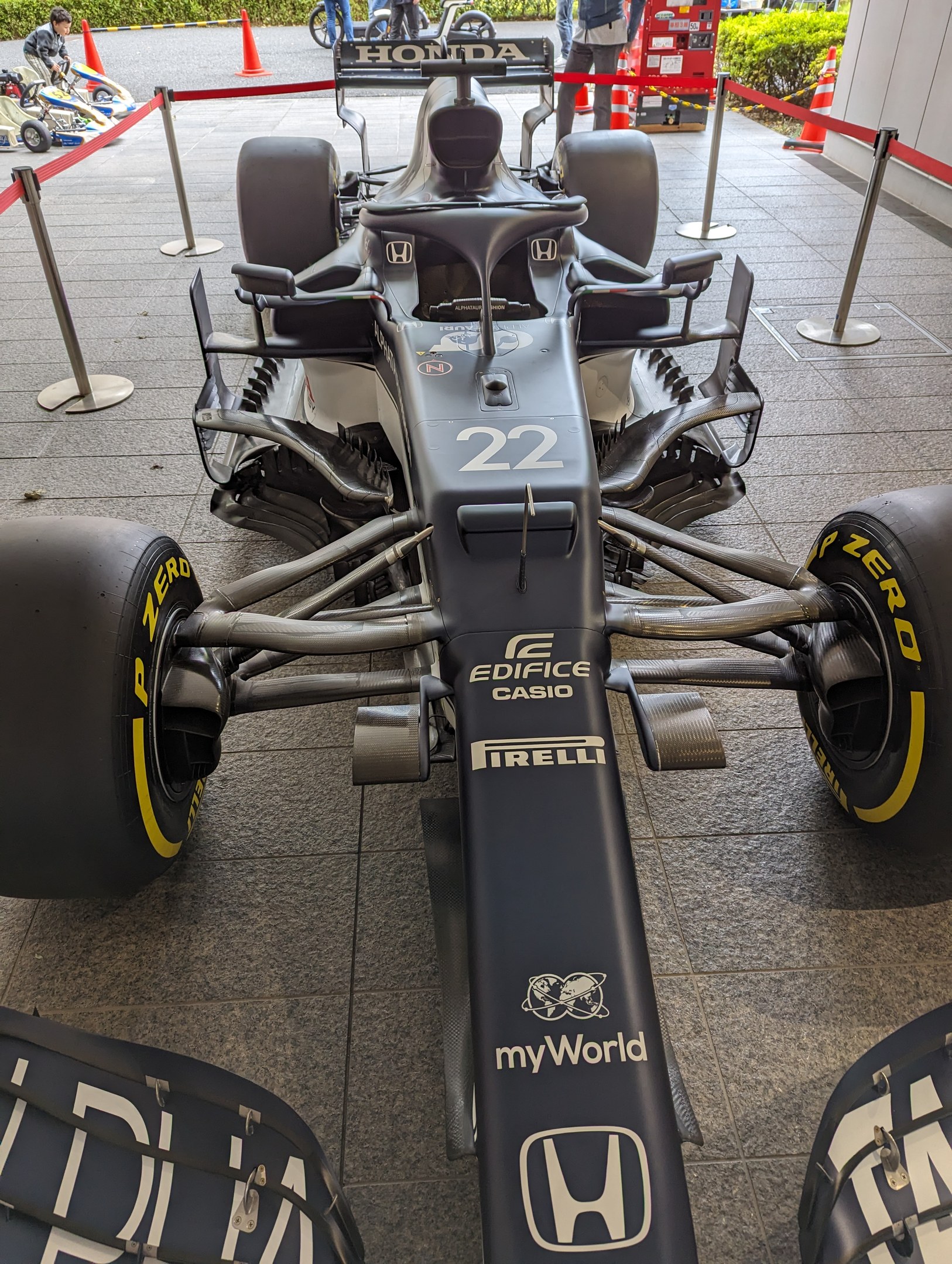 Ein McLaren Mercedes MP4-23 Formel-1-Auto auf der Singapore Grand Prix, umgeben von Barrieren, Verkehrskegeln, Menschen, Fahrzeugen, Pflanzen, Bäumen und einem Gebäude im Hintergrund.