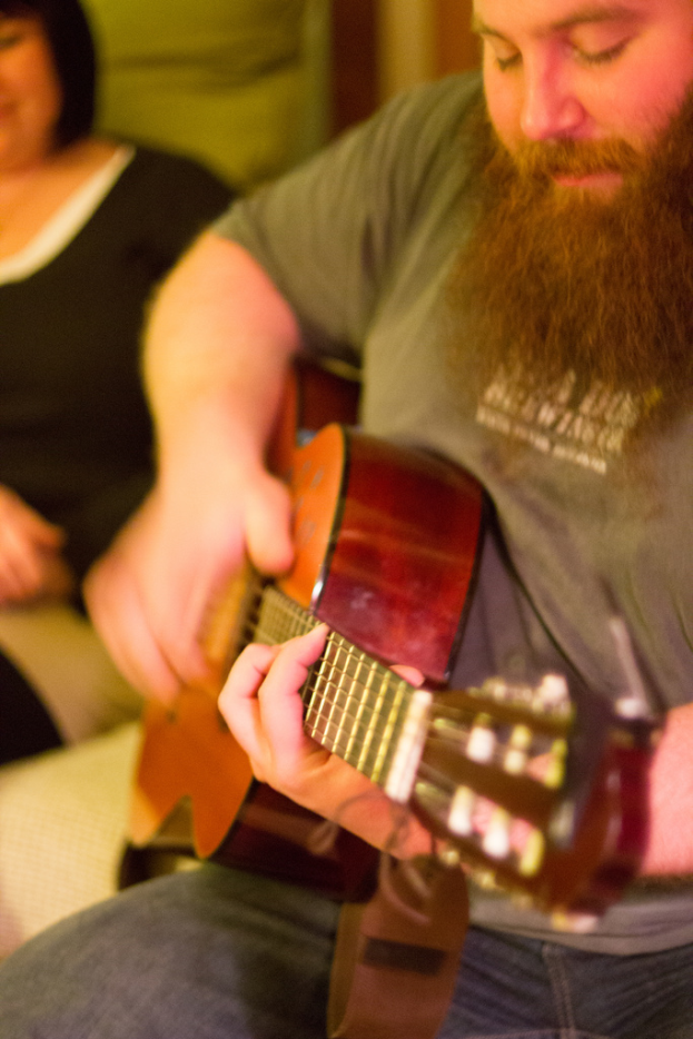 Eine Frau in einem schwarzen Kleid steht neben einem bärtigen Mann mit einer Gitarre auf einem Musikkonzert.