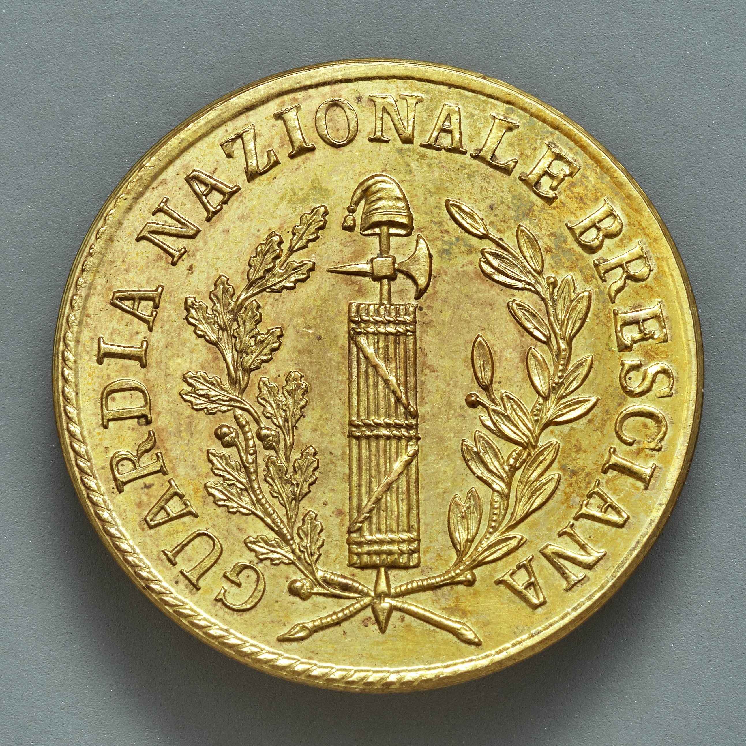 Eine Goldmünze mit der Inschrift "Guardia Nazionale Brescia" auf einem grauen Hintergrund.