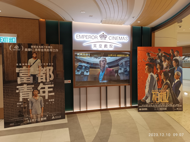 Eintritt zum Emperor Cinemas in Hong Kong mit Bannern, einem Bildschirm, einer Namensplakette, Deckenbeleuchtung und einem Wasserzeichen.