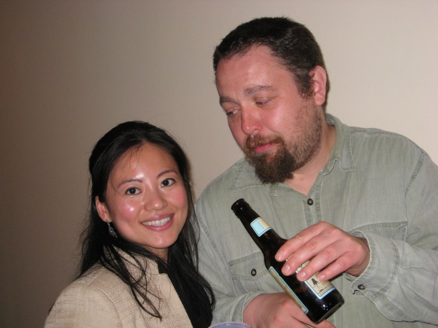 Ein Mann mit einer Flasche schaut eine Frau mit einem Lächeln an, vor einer Wand